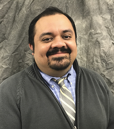 Man with short black hair, goatee, wearing denim short with grey and white striped tie