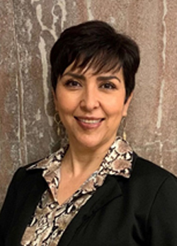 Woman with short black hair wearing a black suit jacket over black and brown floral blouse