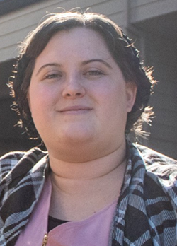 Woman with short brown hair wearing a purple shirt under plaid shirt