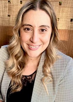 woman with blonde hair wearing a tan checkered jacket over black shirt