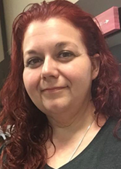 Woman with red hair wearing a gray v-neck with silver necklace