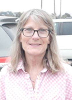 Woman with gray hair wearing precription glasses and a pink polo