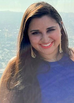 Woman with long, brown hair wearing dangly, gold earrings and a blue sleeveless shirt