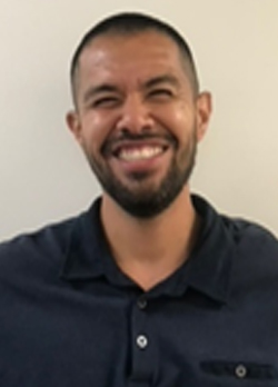 Man with shaved hear and close cropped beard wearing a navy polo