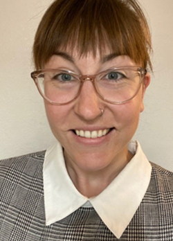Woman with short reddish brown hair wearing prescription glasses and a black checkered blouse with oversized white collar