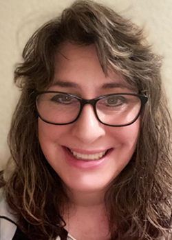 Woman with brown hair wearing glasses and a black, white, pink blouse