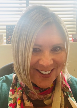 Woman with short blonde hair wearing a green sweater with multi-colored scarf