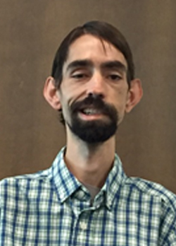 Man with brown hair and goatee wearing a green plaid button up shirt